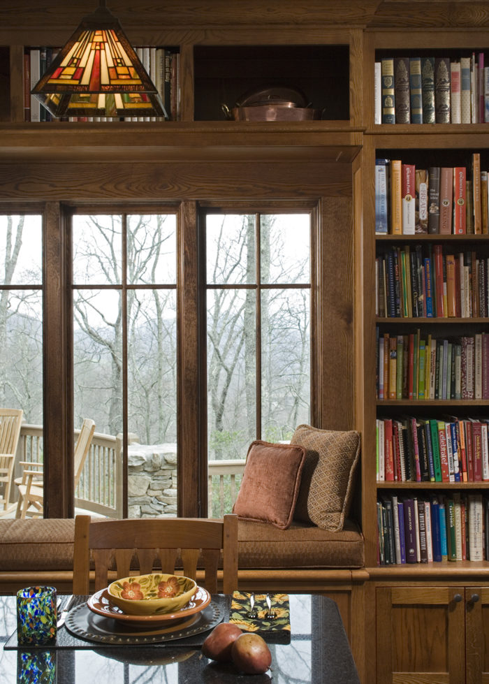 Interior, vertical, kitchen vignette of window seat and bookcase looking out to patio and mountain view, Ossman residence, Sylva, North Carolina, M. Shawn Leatherwood & Associates